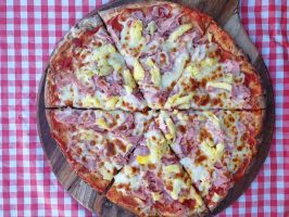Delicious ham and pineapple pizza with melted cheese on a wooden board.